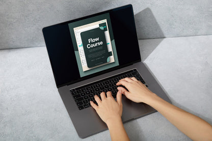 Top-down view of a person typing on a dark gray laptop computer, with the screen displaying a digital course cover titled 'Flow Course'.