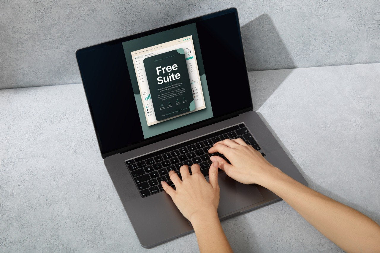 Top-down view of a person typing on a dark gray laptop, with the screen displaying a digital template titled 'Free Suite' against a textured gray background.