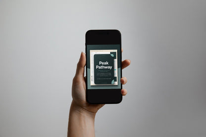 A hand holds a black smartphone against a plain light gray background. The phone screen displays a book or article cover titled 'Peak Pathway'.